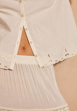 close-up-of-a-cream-colored-eyelet-lace-blouse-with-a-triangular-cutout-at-the-center-front-showing-the-models-midriff-and-a-pleated-matching-skirt
